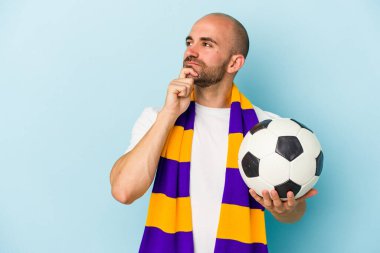 Mavi arka planda izole edilmiş atkı takan genç ve kel bir adam şüpheli ve şüpheci bir ifadeyle yana bakıyor..