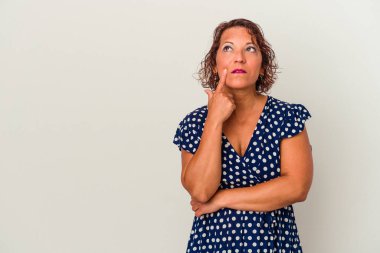 Beyaz arka planda izole edilmiş orta yaşlı Latin kadın şüpheli ve şüpheci bir ifadeyle yana bakıyor..