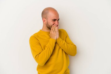 Genç kel adam beyaz arka planda izole edilmiş. Bir şeye gülüyor, elleriyle ağzını kapatıyor..
