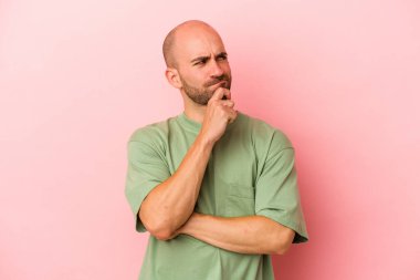Kafkasyalı genç kel adam pembe arka planda izole edilmiş şüpheli ve şüpheci bir ifadeyle yana bakıyor..