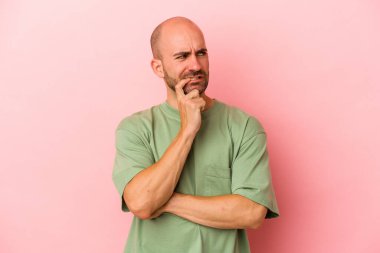 Kafkasyalı genç kel adam pembe arka planda izole edilmiş şüpheli ve şüpheci bir ifadeyle yana bakıyor..