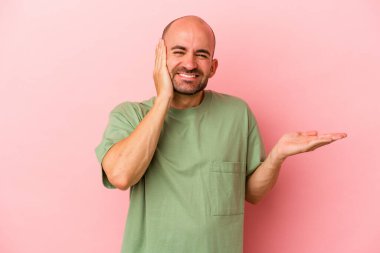 Pembe arka planda izole edilmiş genç, beyaz kel bir adam bir avuç içinde fotokopi alanı tutuyor, el üstünde tutuyor. Şaşırmış ve mutlu..