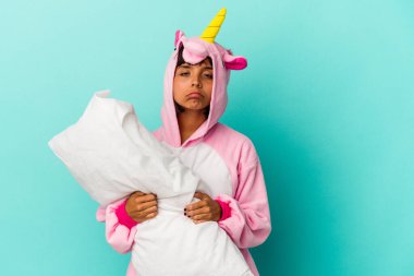 Mavi arka planda bir yastık tutan tek boynuzlu at pijaması giyen genç melez bir kadın.