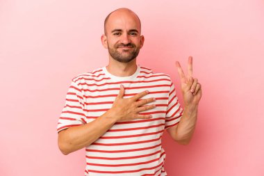 Beyaz saçlı genç adam pembe arka planda izole edilmiş yemin ediyor, elini göğsüne koyuyor..