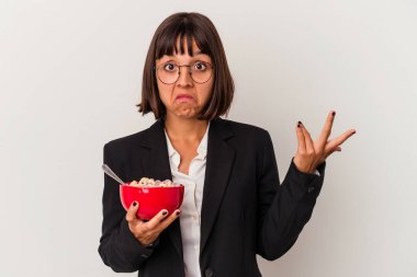 Beyaz arka planda izole edilmiş mısır gevreği yiyen genç bir ırk kadını omuz silker ve gözleri açık kalır..