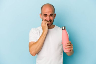 Mavi arka planda kantin tutan genç kel adam tırnaklarını yiyor, gergin ve çok endişeli..