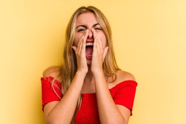 Sarışın, sarı arka planda izole edilmiş genç bir kadın heyecanlı bir şekilde bağırıyor..