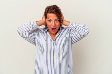 Orta yaşlı Latin bir kadın, beyaz arka planda izole edilmiş kulakları kulaklarıyla kapatıyor ve yüksek sesli sesler duymamaya çalışıyor..