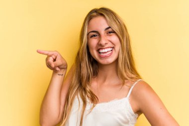 Sarı arka planda izole edilmiş, neşeli gülümseyen, işaret parmağıyla işaret eden beyaz saçlı genç bir kadın..