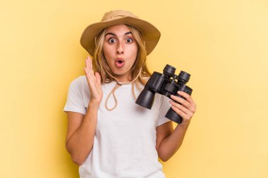 Sarı arka planda dürbün tutan genç beyaz kadın şaşırdı ve şok oldu..