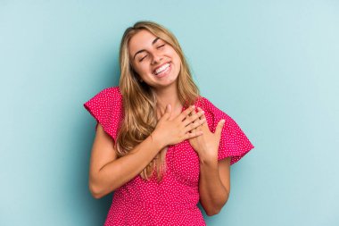 Mavi arka planda izole edilmiş beyaz tenli genç bir kadın, dostane bir ifadeye sahip, avuçlarını göğsüne bastırıyor. Aşk konsepti.