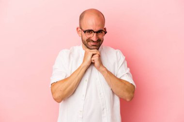 Pembe arka planda izole edilmiş genç beyaz kel adam ellerini çenesinin altında tutuyor, mutlu bir şekilde yana bakıyor..