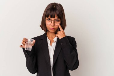 Genç melez iş kadını elinde bir bardak su tutarak beyaz arka planda izole edilmiş bir şekilde şakağı işaret ediyor, düşünüyor ve bir göreve odaklanıyor..