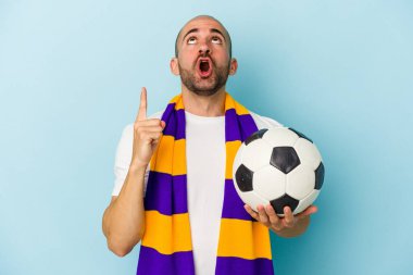 Mavi arka planda izole edilmiş atkı takan genç ve kel bir adam ağzı açık, üst tarafı işaret ediyor..