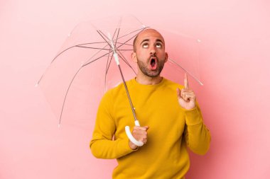 Pembe arka planda şemsiyesi olan beyaz, kel bir adam ağzı açık, üst tarafı işaret ediyor..