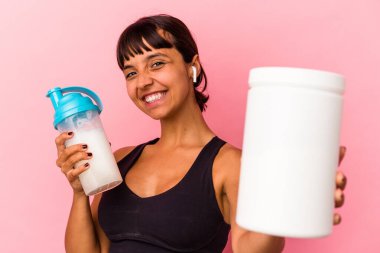 Genç melez kadın pembe arka planda izole edilmiş protein içeceği içiyor.