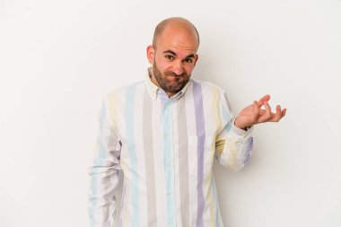 Genç kel adam, beyaz arka planda izole edilmiş. Şüpheyle bakıyor ve sorgulama sırasında omuzlarını silkiyor..