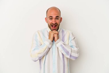 Genç kel adam beyaz arka planda izole edilmiş şans için dua ediyor, şaşkın ve ağzı açık bir şekilde önüne bakıyor..
