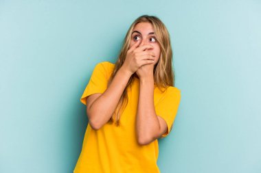 Beyaz tenli sarışın kadın mavi arka planda izole edilmiş. Düşünceli bir şekilde bir fotokopi odasına bakıyor. Ağzını eliyle kapatıyor..