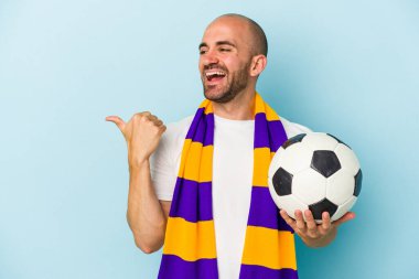 Mavi arka plan noktalarına izole edilmiş atkı takan genç ve kel bir adam başparmak uzakta, gülüyor ve kaygısız..