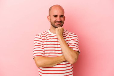 Genç beyaz kel adam pembe arka planda izole edilmiş mutlu ve kendinden emin gülümsüyor, elleriyle çenesine dokunuyor..