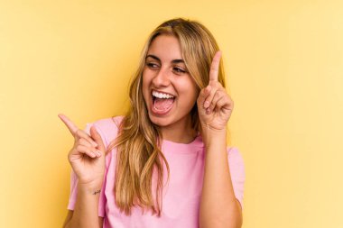 Sarı arka planda izole edilmiş genç beyaz kadın farklı kopya alanlarını gösteriyor, birini seçiyor, parmaklarıyla gösteriyor..