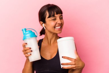 Genç melez kadın pembe arka planda izole edilmiş protein içeceği içiyor.