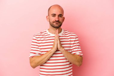 Kafkasyalı genç kel adam pembe arka planda izole edilmiş dua ediyor, bağlılık gösteriyor, dindar biri ilahi ilham arıyor..