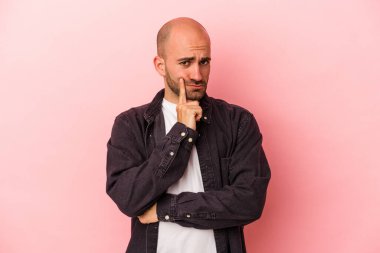 Kafkasyalı genç kel adam pembe arka planda izole edilmiş şüpheli ve şüpheci bir ifadeyle yana bakıyor..