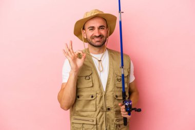 Genç, kel bir balıkçı pembe arka planda izole edilmiş bir çubuk tutuyor neşeli ve kendinden emin..