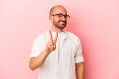 Genç beyaz kel adam pembe arka planda izole edilmiş neşeli ve kaygısız parmaklarıyla barış sembolü gösteriyor..