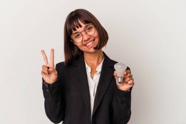 Genç melez iş kadını beyaz arka planda izole edilmiş bir ampul tutuyor neşeli ve kaygısız parmaklarıyla barış sembolü gösteriyor..