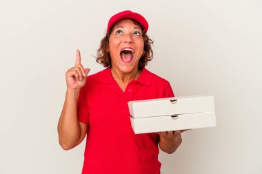 Orta yaşlı teslimatçı kadın beyaz arka planda izole edilmiş pizzaları alıp ağzı açık bir şekilde üst tarafı işaret ediyor..