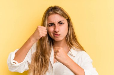 Sarışın, sarışın bir kadın sarı arka planda izole edilmiş. Yumruk atıyor, sinirleniyor, kavga ediyor..