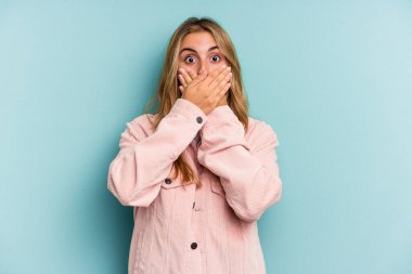Mavi arka planda izole edilmiş beyaz, sarışın genç bir kadın elleriyle ağzını kapatırken şok oldu..