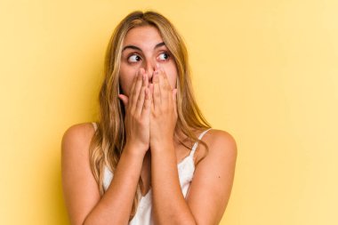 Sarışın, sarı arka planda izole edilmiş genç, beyaz bir kadın. Elle ağzını kapatan bir fotokopi odasına bakıyor..