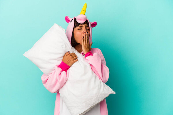 Young mixed race woman wearing a unicorn pajama holding a pillow isolated on blue background