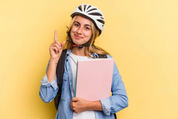 若いですCaucasian学生女性身に着けていますAバイクヘルメット絶縁上の黄色の背景ショーナンバーワンとともに指 — ストック写真
