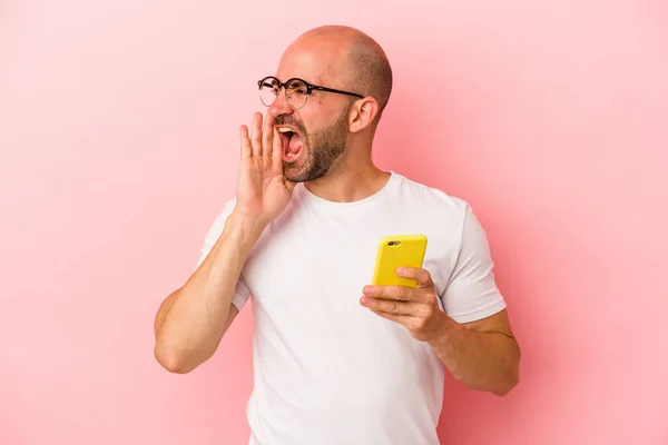 Młody Biały Łysy Człowiek Trzymając Telefon Komórkowy Odizolowany Różowym Tle — Zdjęcie stockowe