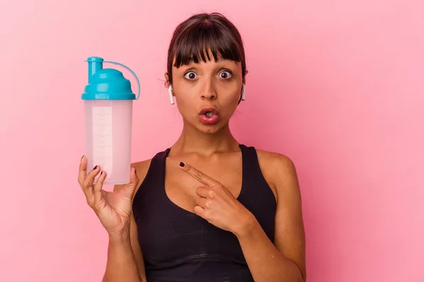 若い混合人種の女性は タンパク質を飲む側を指してピンクの背景に隔離された振る — ストック写真