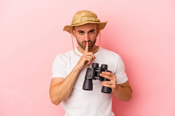 年轻的高加索秃头男子手持双筒望远镜 与粉色背景隔离 保守秘密或要求沉默 — 图库照片