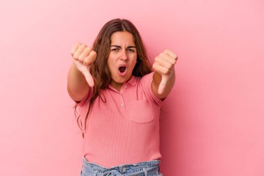 Pembe arka planda izole edilmiş genç beyaz kadın baş parmağını aşağı gösteriyor ve hoşlanmadığını ifade ediyor..
