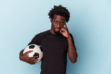 Amerikan futbolu oynayan genç Afro-Amerikan adam mavi arka planda izole edilmiş, parmağıyla şakağı işaret ediyor, düşünüyor, bir göreve odaklanıyor..