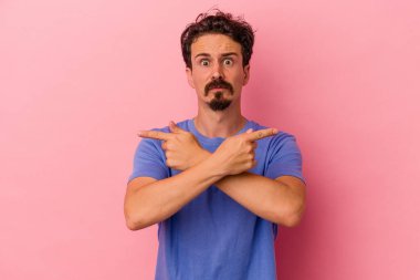 Pembe arka plan noktalarında izole edilmiş genç beyaz adam iki seçenek arasında seçim yapmaya çalışıyor..