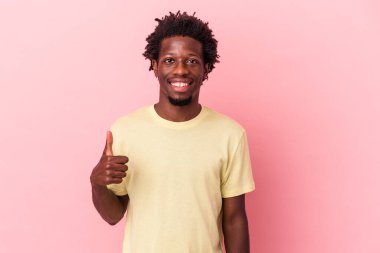Genç Afrikalı Amerikalı adam pembe arka planda izole edilmiş gülümsüyor ve başparmağını kaldırıyor.