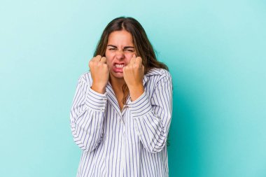 Mavi arka planda izole edilmiş genç beyaz kadın yumruğunu kameraya gösteriyor, agresif yüz ifadesi..