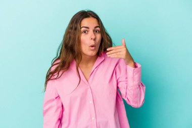 Mavi arka planda izole edilmiş genç beyaz kadın bir şeye gülüyor, elleriyle ağzını kapatıyor..