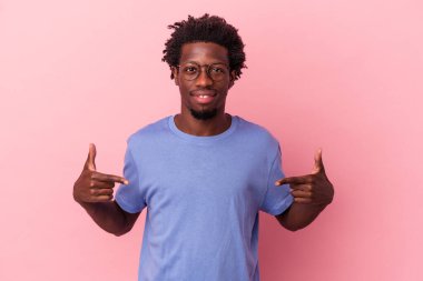 Genç Afro-Amerikalı bir adam pembe arka planda izole edilmiş. Elle bir tişört fotokopisini gösteriyor. Gururlu ve kendinden emin.