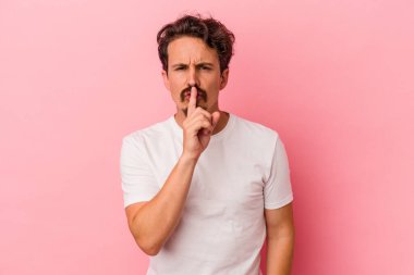 Pembe arka planda izole edilmiş genç beyaz bir adam ya sır saklıyor ya da sessizlik istiyor..