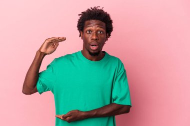Genç Afrikalı Amerikalı bir adam pembe arka planda izole edilmiş iki eliyle bir şey tutuyor, ürün sunumu..